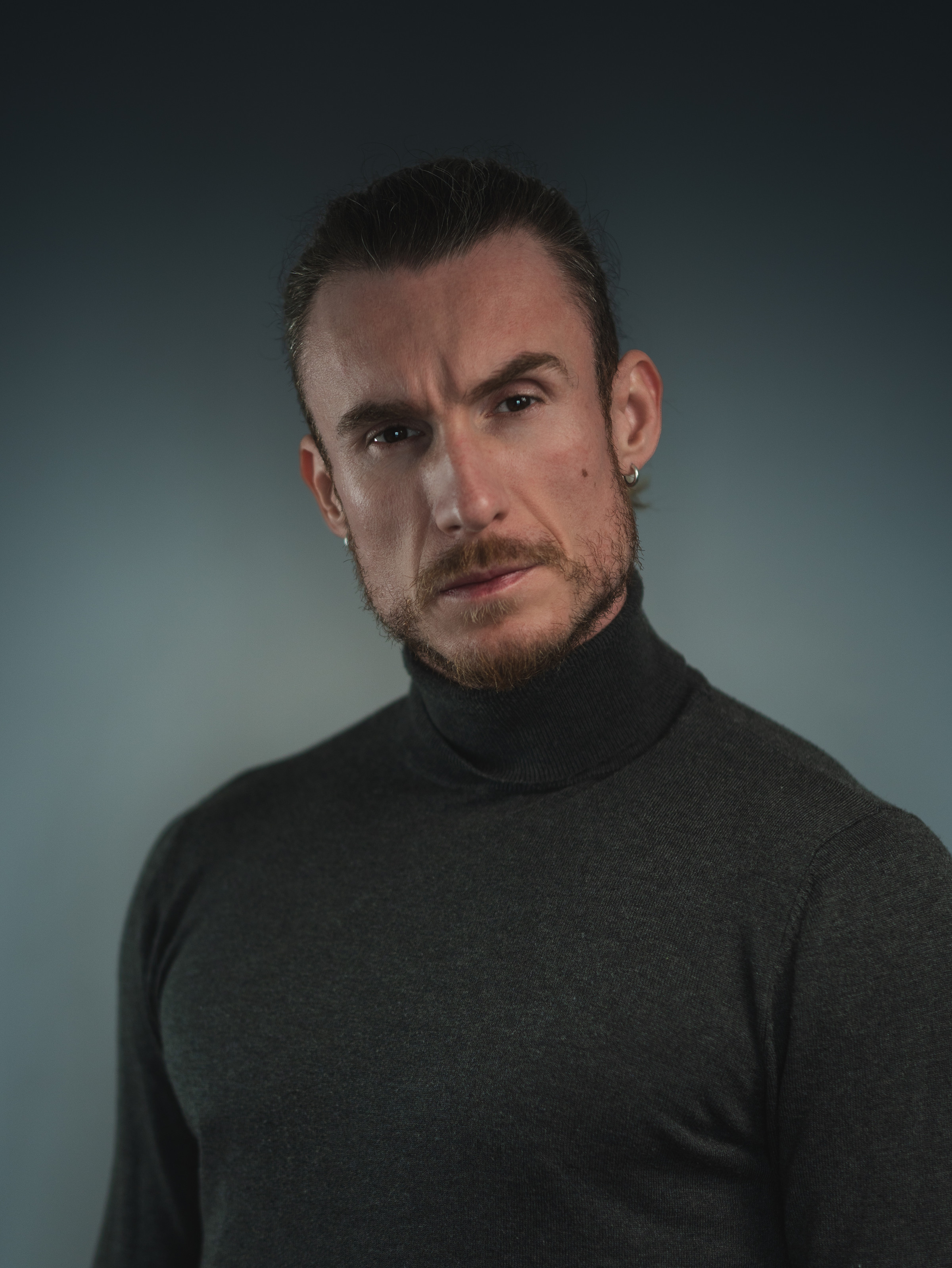 Adi Gheo neutral casting headshot in a black turtleneck with long hair tied back