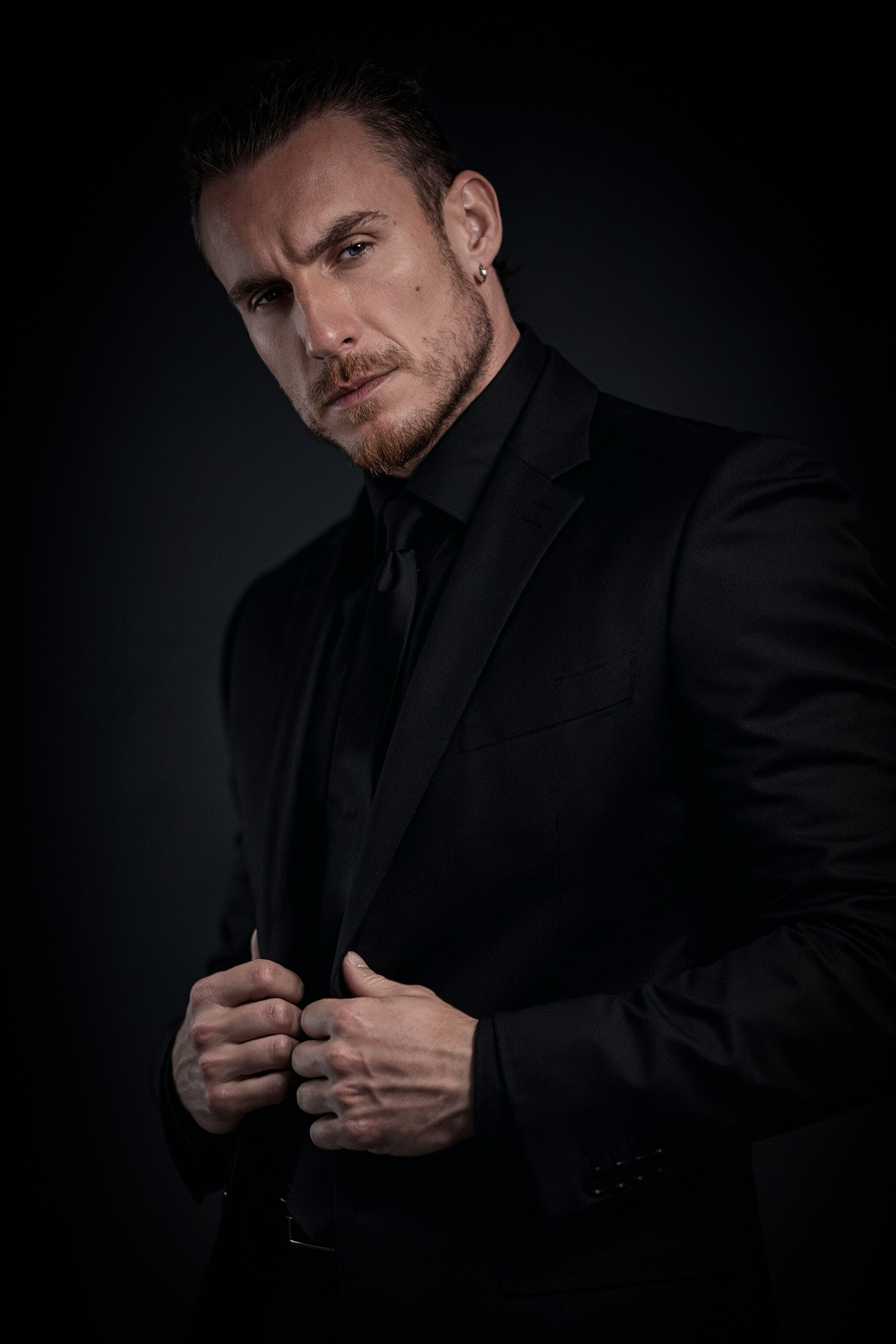 Adi Gheo cinematic portrait in a black suit with long hair tied back