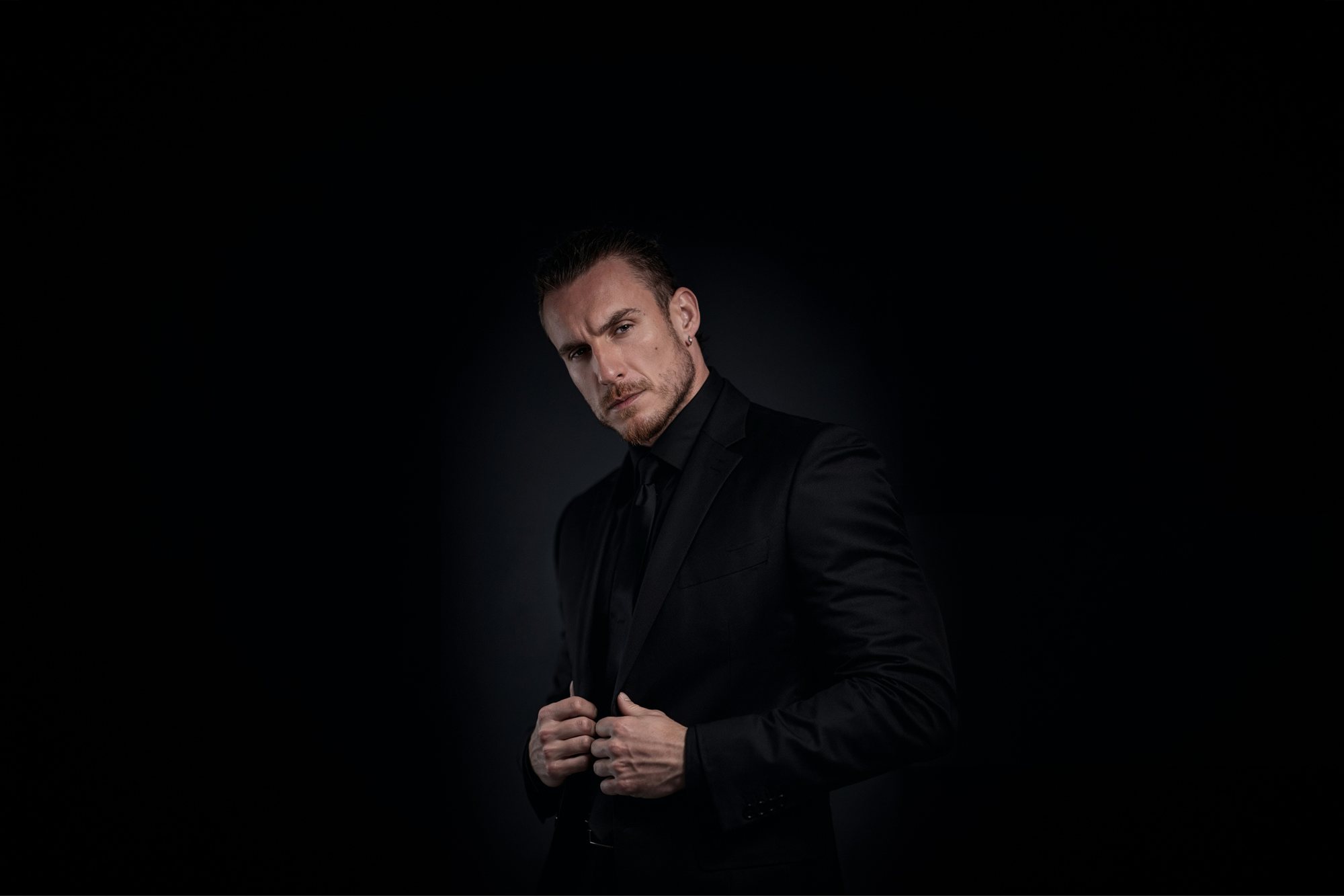 Adi Gheo holding his black suit jacket in a dark studio portrait