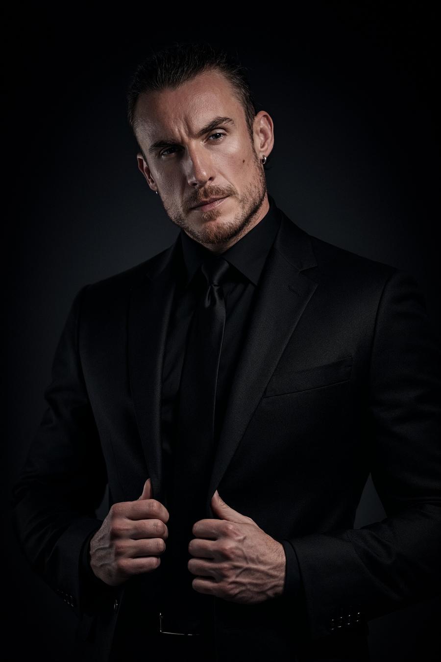 Adi Gheo in a black suit, shirt and tie against a dark backdrop