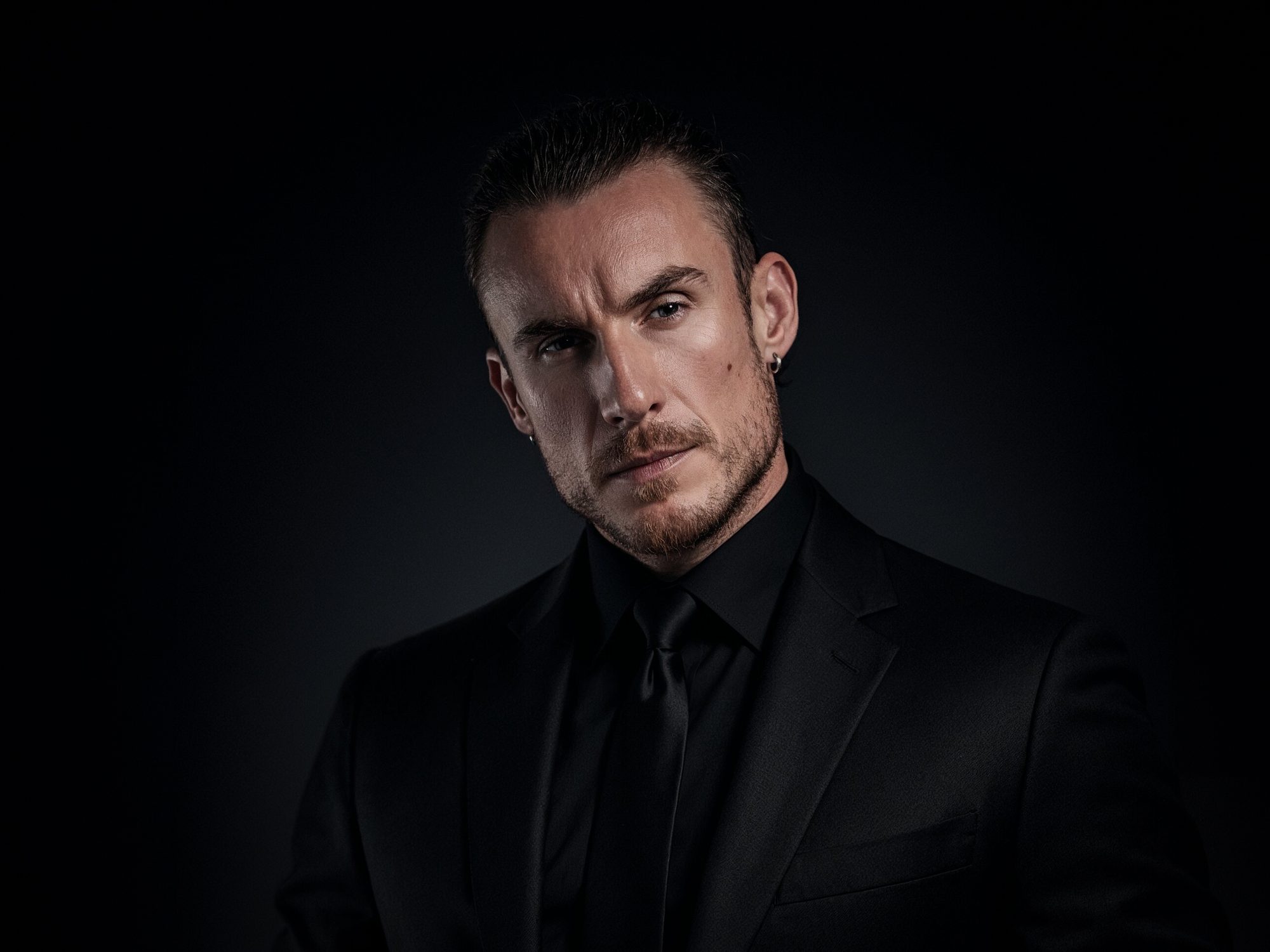 Adi Gheo in a black suit and tie against a dark backdrop, color homepage portrait